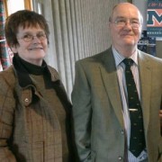 Smiling woman with short dark hair and glasses next to a smiling balding man with glasses